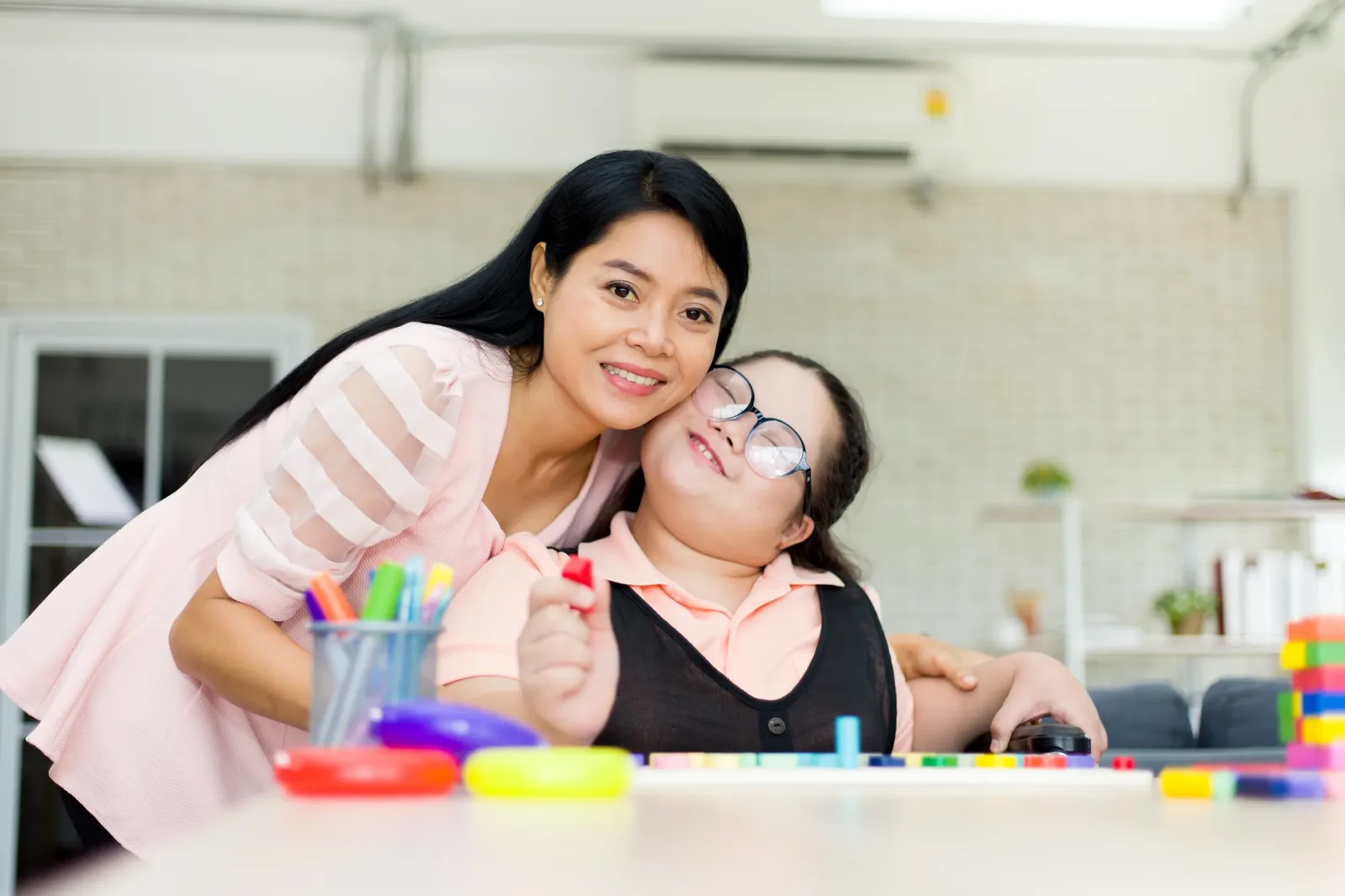 Caregiver hugging child with special needs at learning table